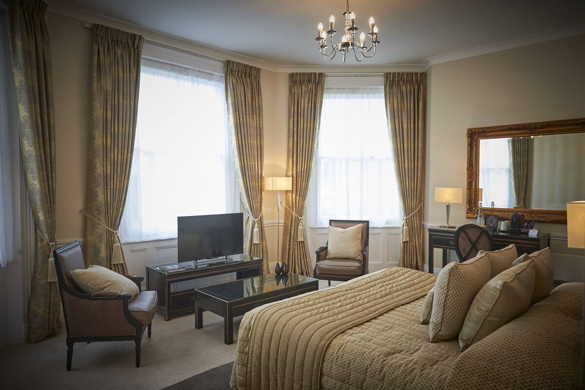 A hotel room with a large bed, a television, a desk, and two chairs.