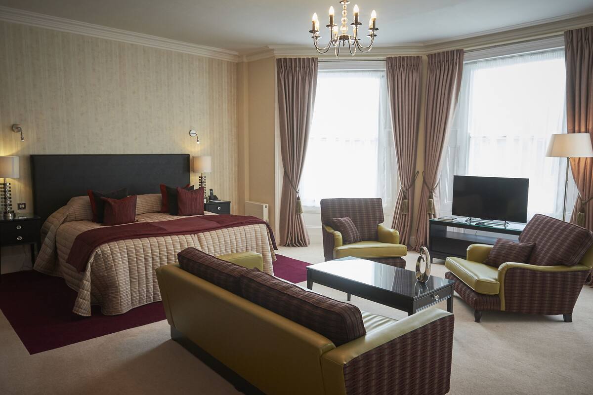 A hotel room with a large bed, a sofa, a television, and a desk.