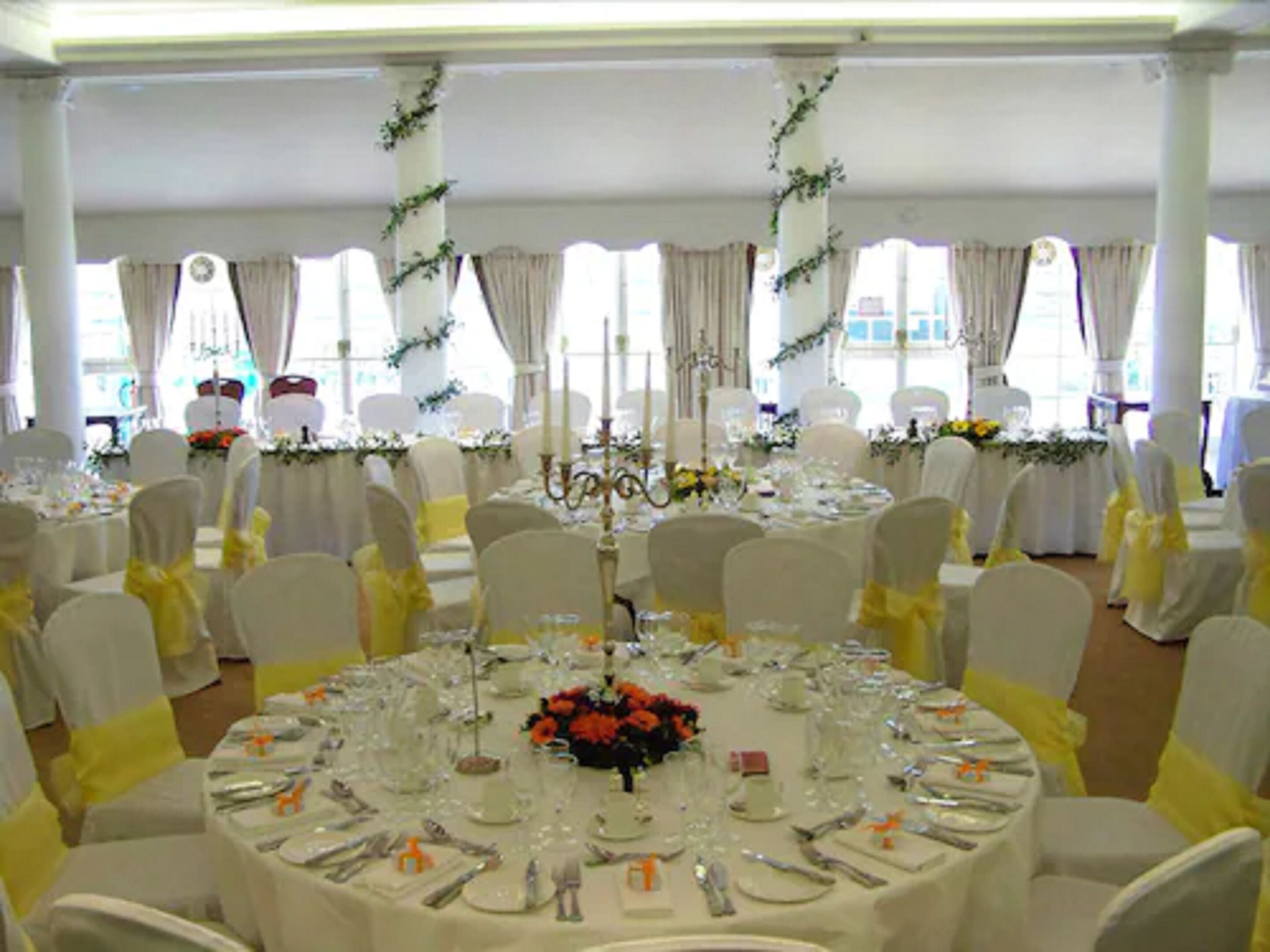 A banquet hall with round tables set for a formal event, decorated with white tablecloths and yellow sashes.