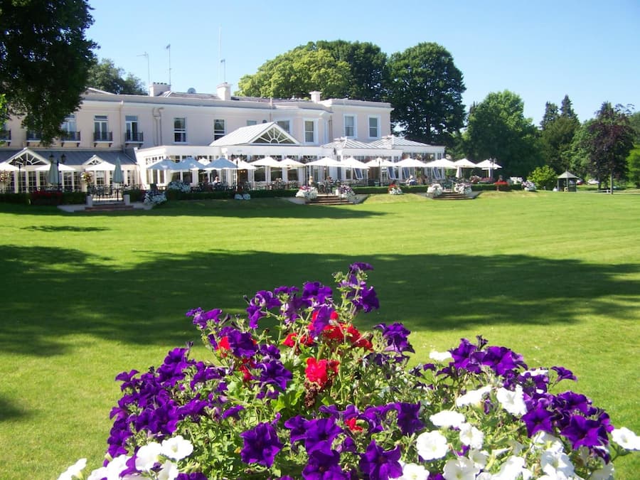 Un grand bâtiment, avec de nombreuses tentes blanches et des tables disposées sur une pelouse, ce qui laisse supposer qu’un événement ou une réception en plein air est en cours.