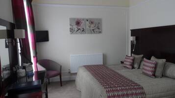 A hotel room with a bed, a desk, a chair, a radiator, and two wall-mounted artworks.