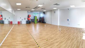 A spacious indoor gym with wooden flooring, exercise equipment, and a large mirror.
