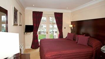 Habitación de hotel con una cama grande, televisión y vistas a un jardín por la ventana.
