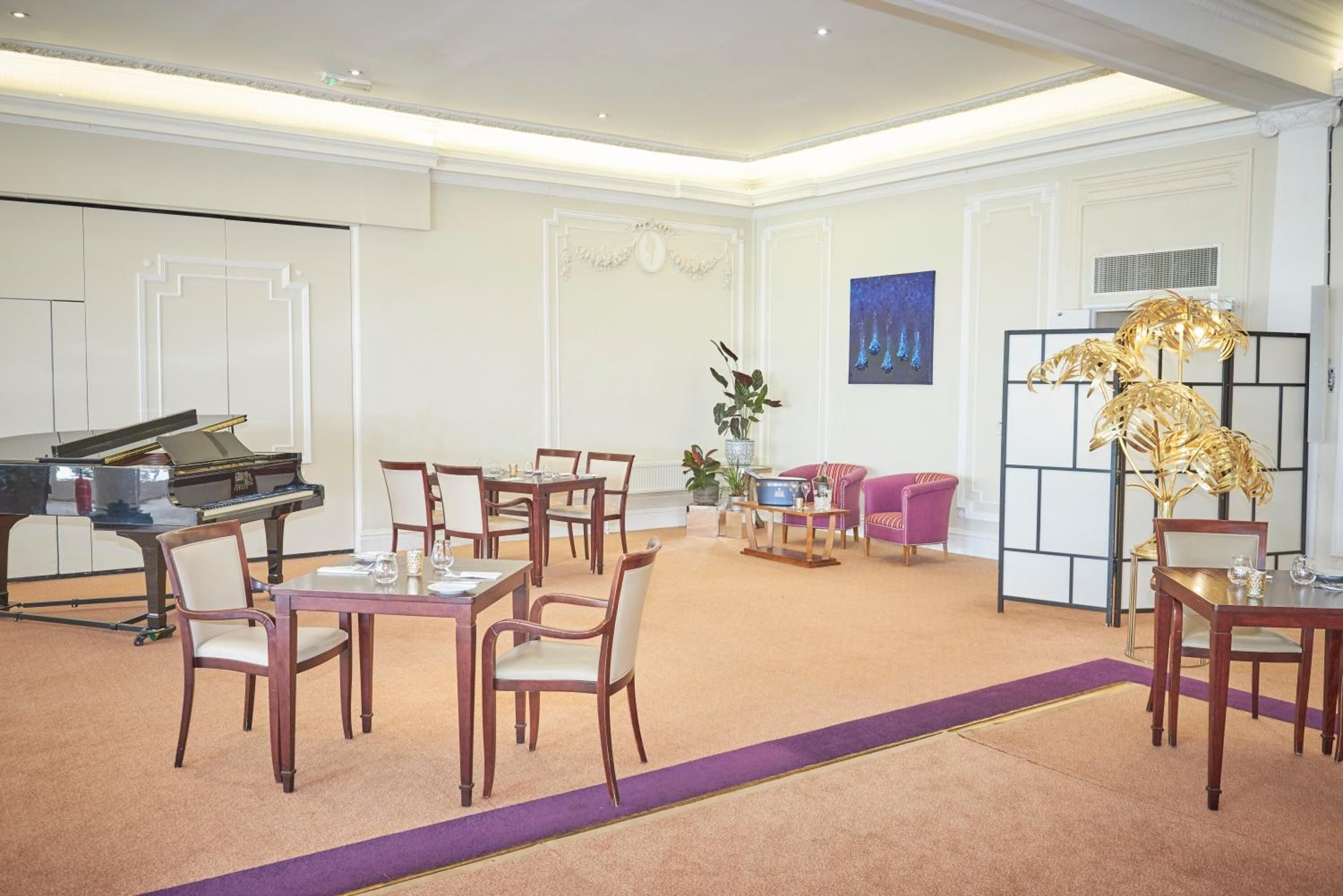 A spacious room with a grand piano, multiple dining tables, and chairs, a decorative plant, and a large abstract painting on the wall.