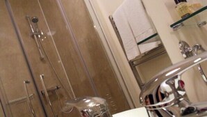Een badkamer met een douchecabine van glas, een wit wastafeltje en een spiegel.
