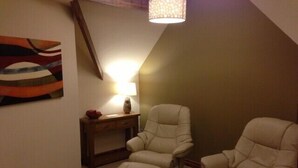 Een kamer met twee leren fauteuils, een klein houten bijzettafeltje met een lamp, en een kleurrijk abstract schilderij aan de muur.