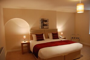 A bedroom with a large bed, two bedside tables, a wall-mounted artwork, and a hanging light fixture. - The Port House (Morecambe)