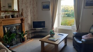 Una sala de estar con chimenea, un televisor sobre una mesa de vidrio, un sofá y una ventana con cortinas.