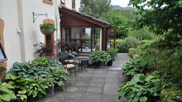 Un patio cubierto con plantas en macetas, muebles de exterior y vistas a una colina.