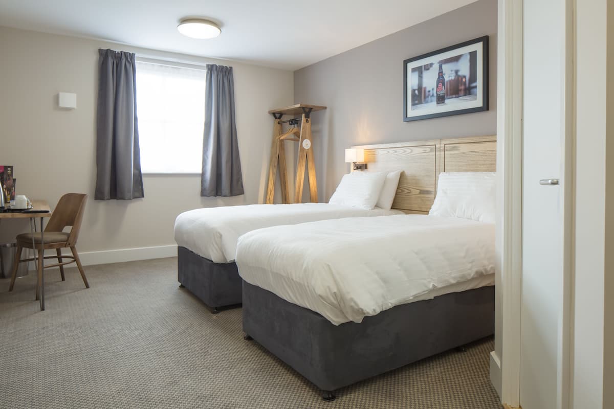 Une chambre d’hôtel avec deux lits, un bureau, une chaise et une fenêtre avec des rideaux.