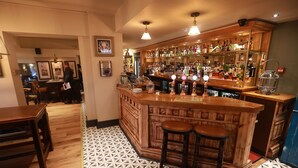 A bar area with a wooden counter, stools, and a patterned floor. - Green Lodge, Wirral by Marston's Inns (Wirral)