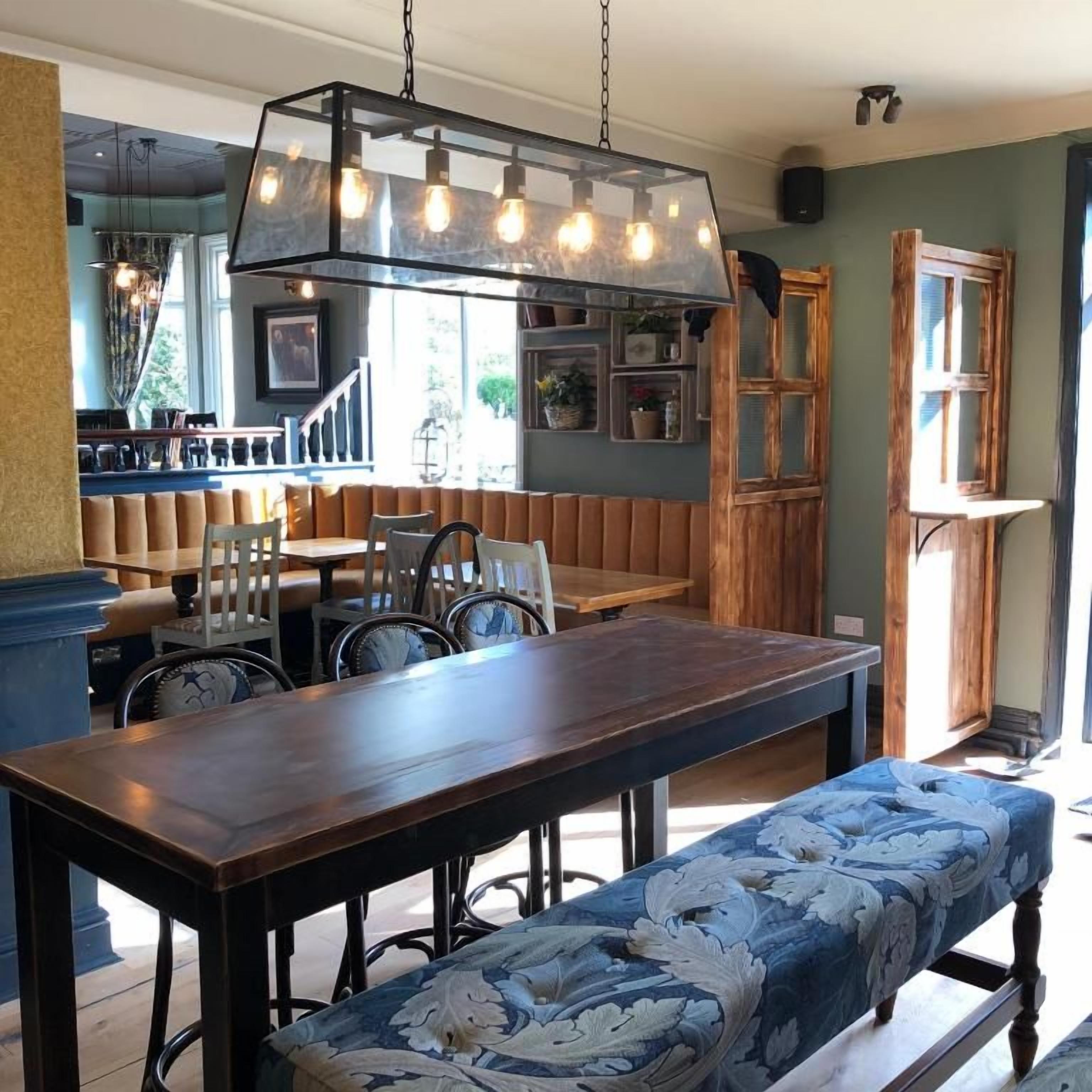 Uma sala de jantar com mesa e banco de madeira, luminária pendente e vista para o exterior.
