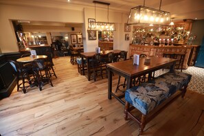 A bar area with wooden furniture, a bar counter, and a hanging light fixture. - Green Lodge, Wirral by Marston's Inns (Wirral)