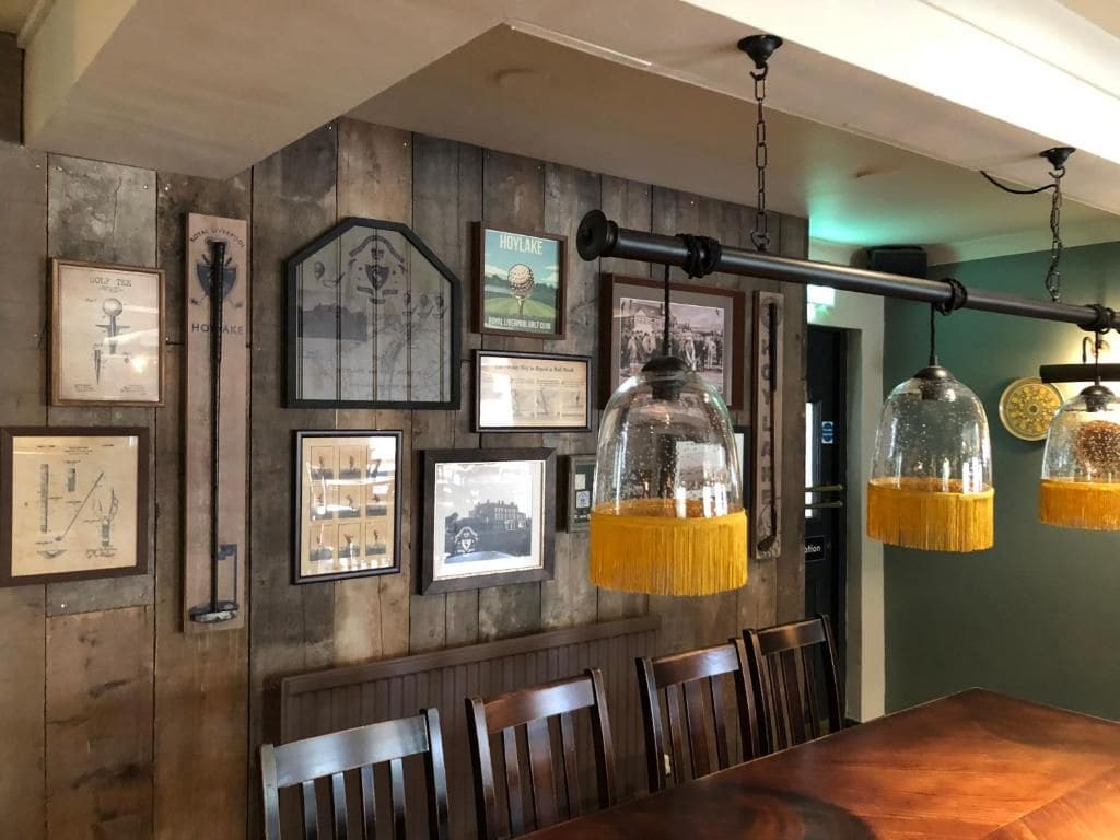 A dining area with a wooden wall, framed pictures, and hanging pendant lights.