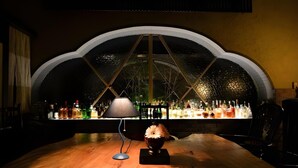 A bar area with a large arched window, a table with a lamp, and a variety of bottles. - Ryokan Sugimoto (Matsumoto)