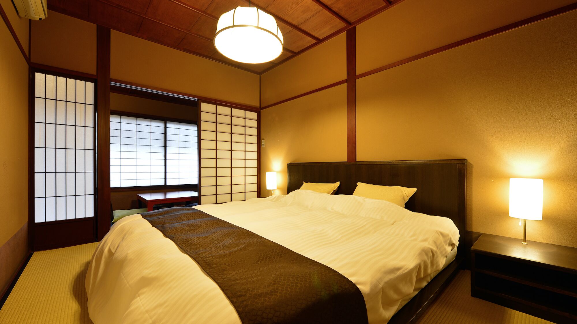 Een traditionele Japanse slaapkamer met tatami vloeren, een laag houten bed, shoji schermen en een hanglamp.
