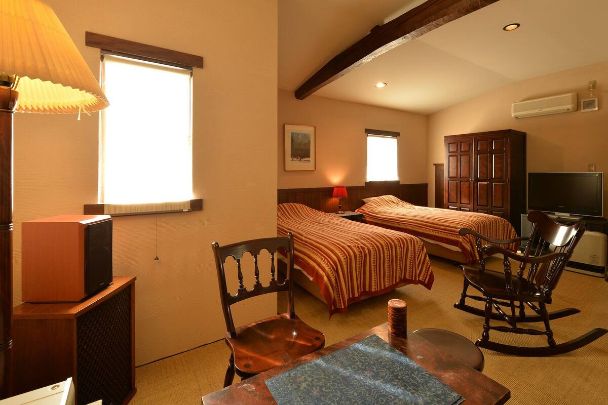 Une chambre d’hôtel avec deux lits, une télévision, un bureau avec une chaise et une lampe.