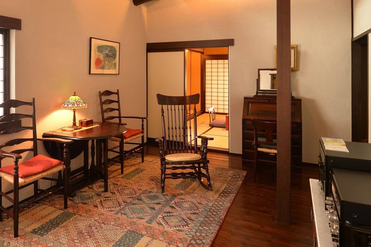 Une pièce de style japonais traditionnel, avec un sol recouvert de tatamis, une table basse, des chaises en bois, une lampe et un piano.