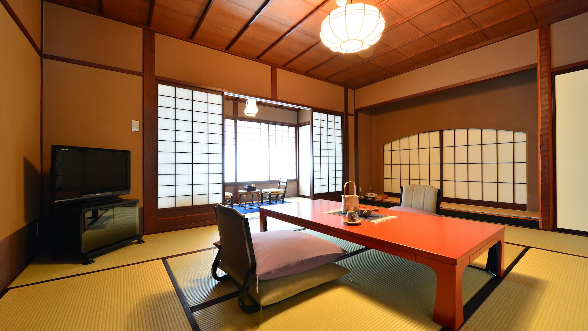 Een traditionele Japanse kamer met tatami vloerbedekking, een televisie, een tafel met kussen, en schuifdeuren voorzien van shoji schermen.