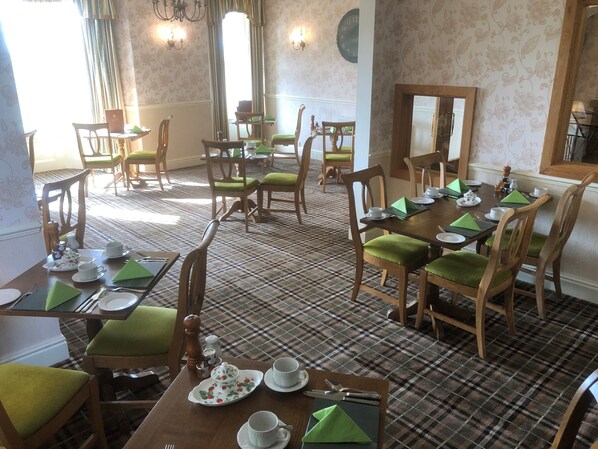 A dining area with checkered flooring, green upholstered chairs, and tables set with white plates, cups, and green napkins.