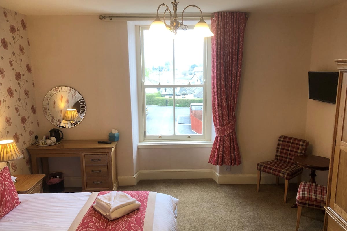 Une chambre d’hôtel avec un lit, un bureau, une chaise, un miroir et une fenêtre avec des rideaux.