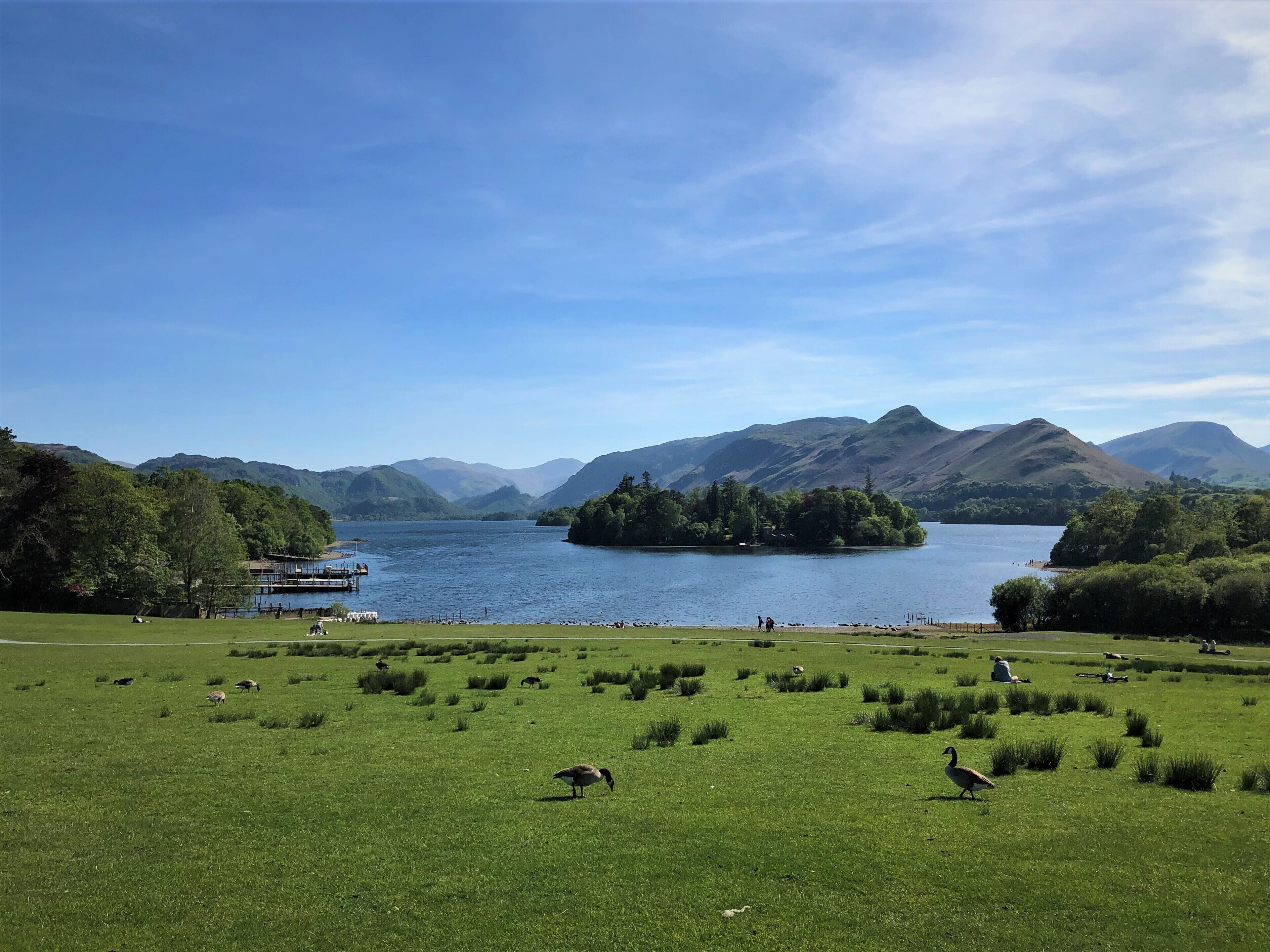 Une vue pittoresque d’un lac entouré de montagnes, avec un champ verdoyant au premier plan et une jetée sur le lac.