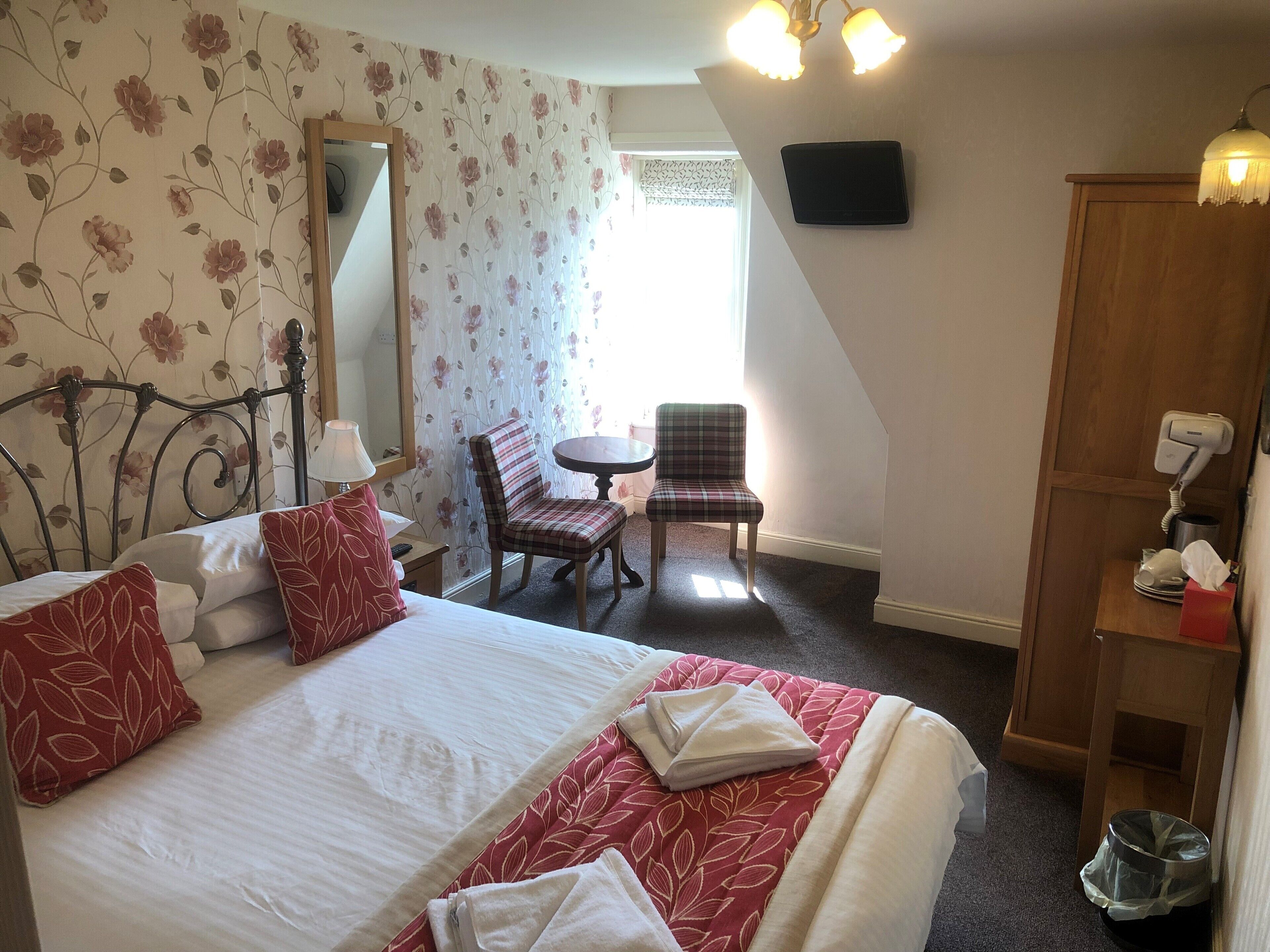 A hotel room with a bed, a chair, a small table, a mirror, and a wardrobe.