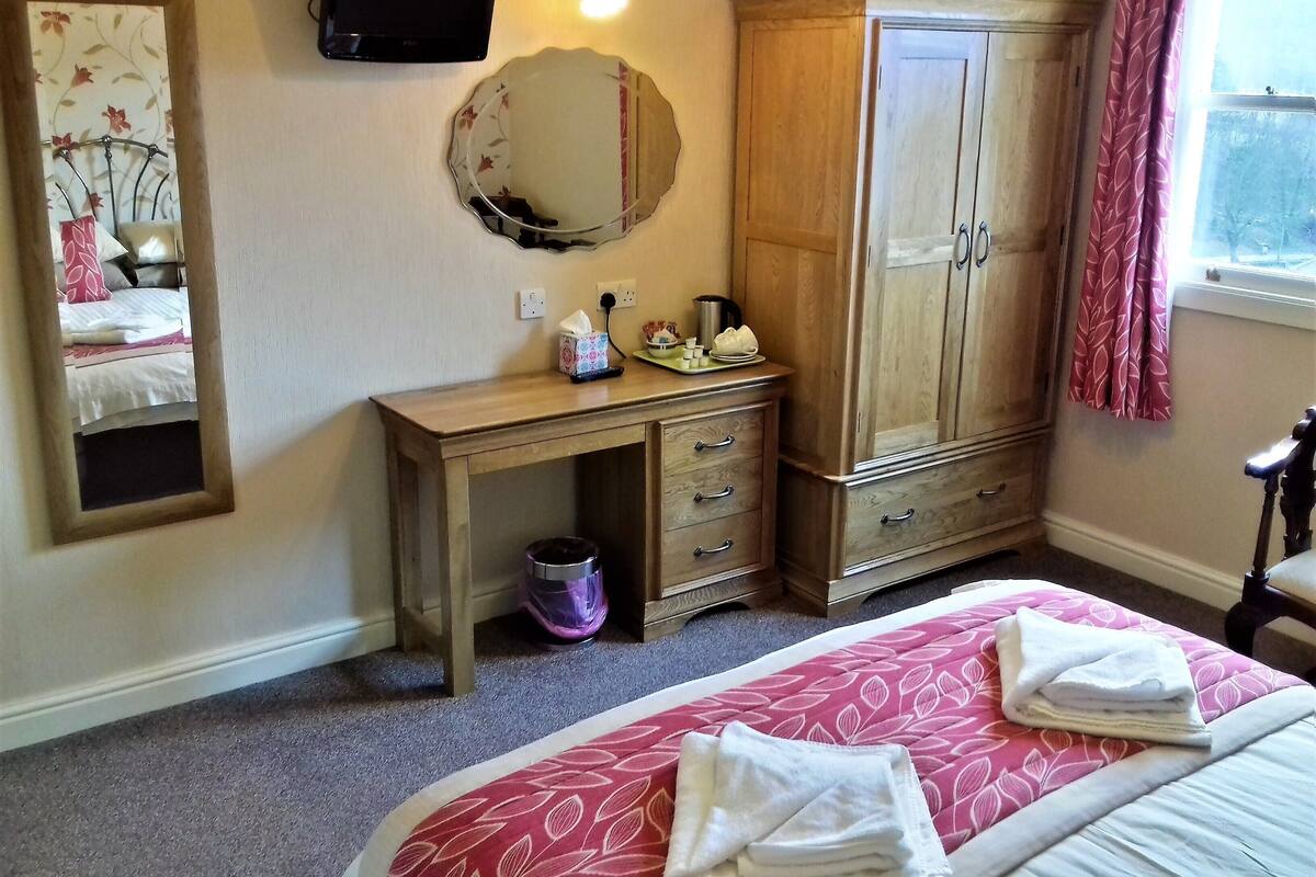 Une chambre à coucher avec un lit, une armoire en bois, un bureau avec un miroir et un téléviseur fixé au mur.