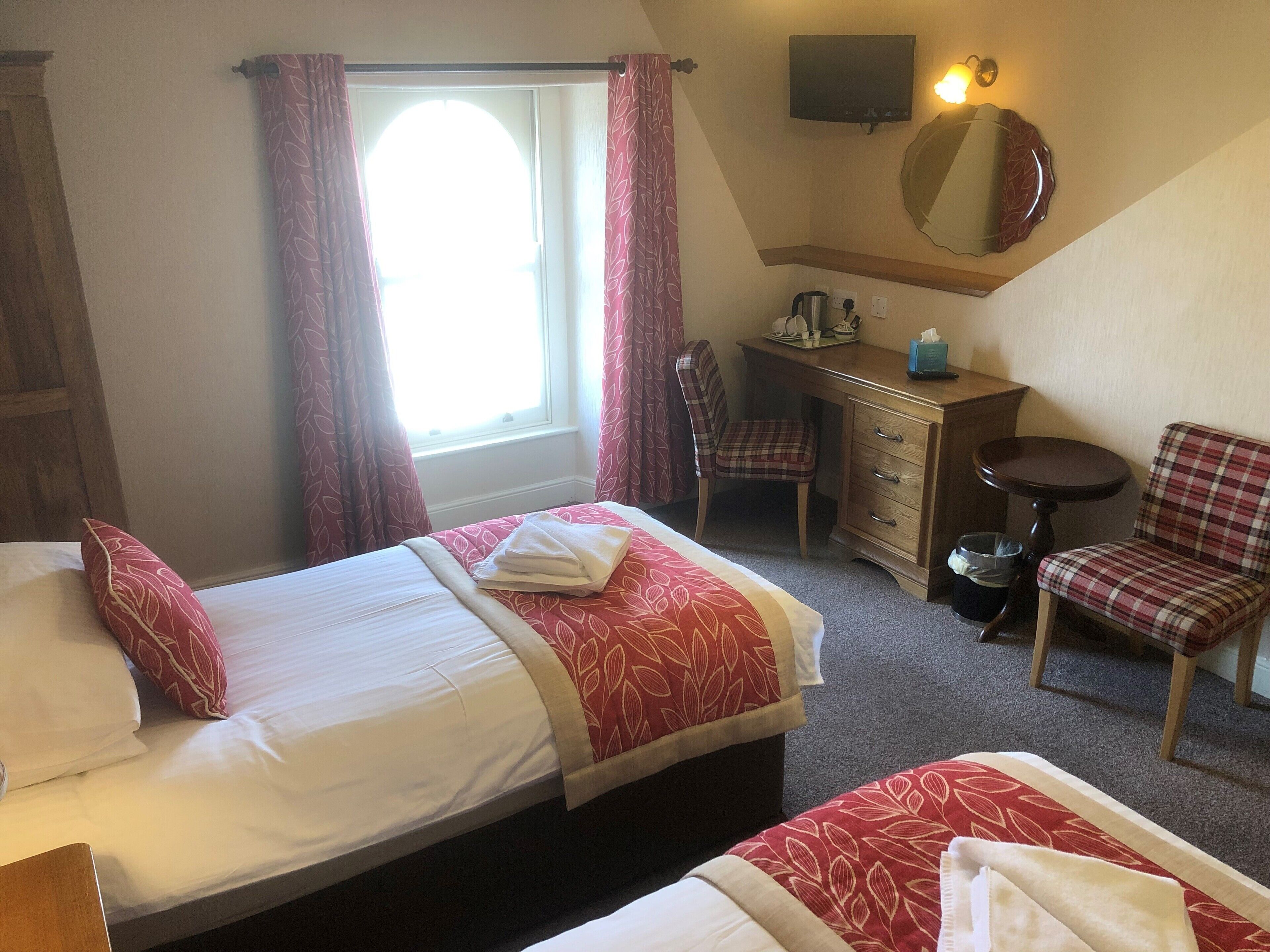 Habitación de hotel con dos camas, un escritorio, una silla, un televisor y una ventana con cortinas.