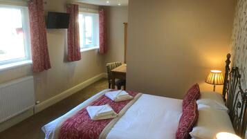 A hotel room with a bed, a chair, a table, a lamp, and a TV on the wall.