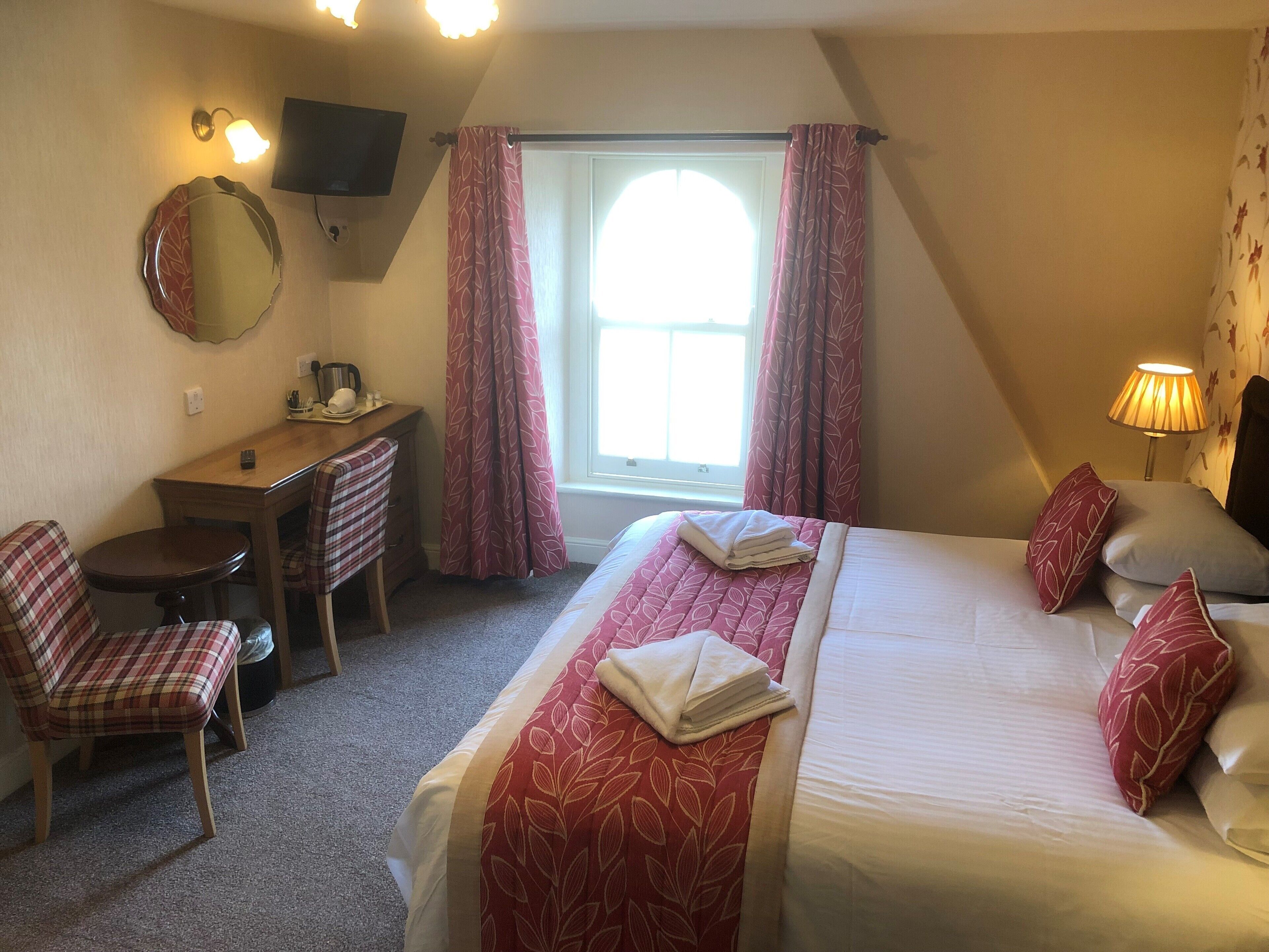 Ein Hotelzimmer mit einem Bett, einem Schreibtisch, einem Stuhl, einem Fernseher und einem Fenster mit Vorhängen.
