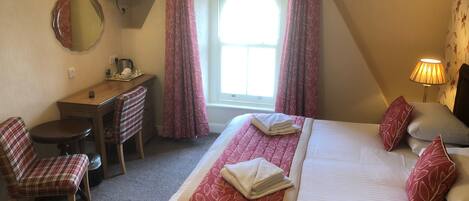 A hotel room with a bed, a desk, a chair, a television, and a window with curtains.