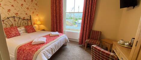 A hotel room with a bed, a chair, a desk, a television, and a window with curtains.