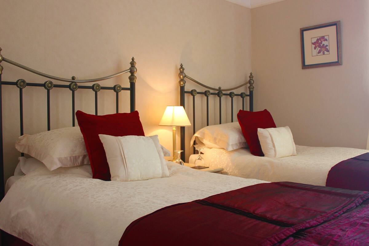 A double bed with a red and white bedspread, a nightstand with a lamp, and a framed picture on the wall.