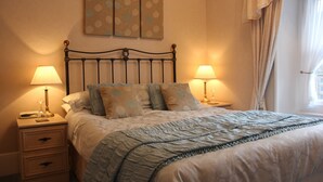A neatly made bed with a patterned bedspread, two bedside lamps, a nightstand with drawers, and a wall with two framed artworks. - Tarn Hows Guest House (Keswick)