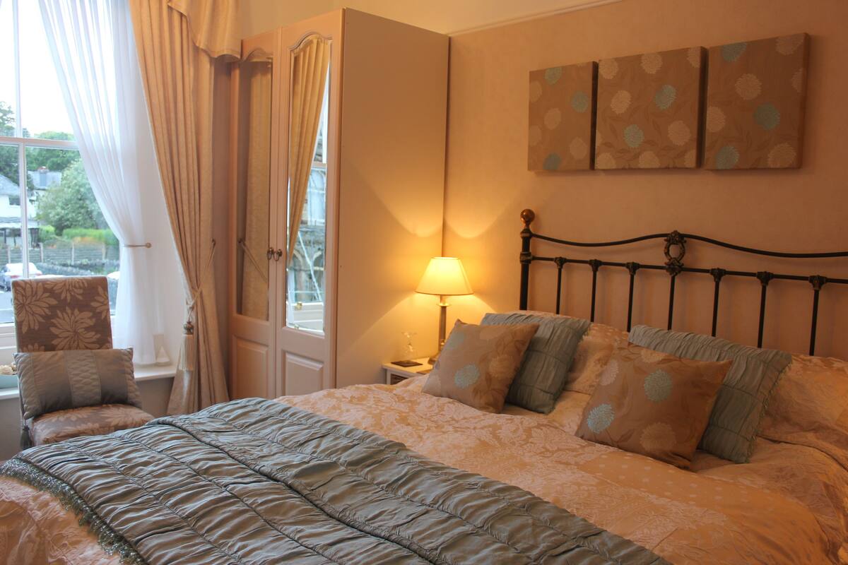 A bedroom with a bed, a nightstand, a lamp, and a window with curtains.