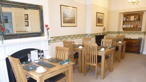 A dining area with wooden tables and chairs, a fireplace, and framed artwork on the walls. - Tarn Hows Guest House (Keswick)