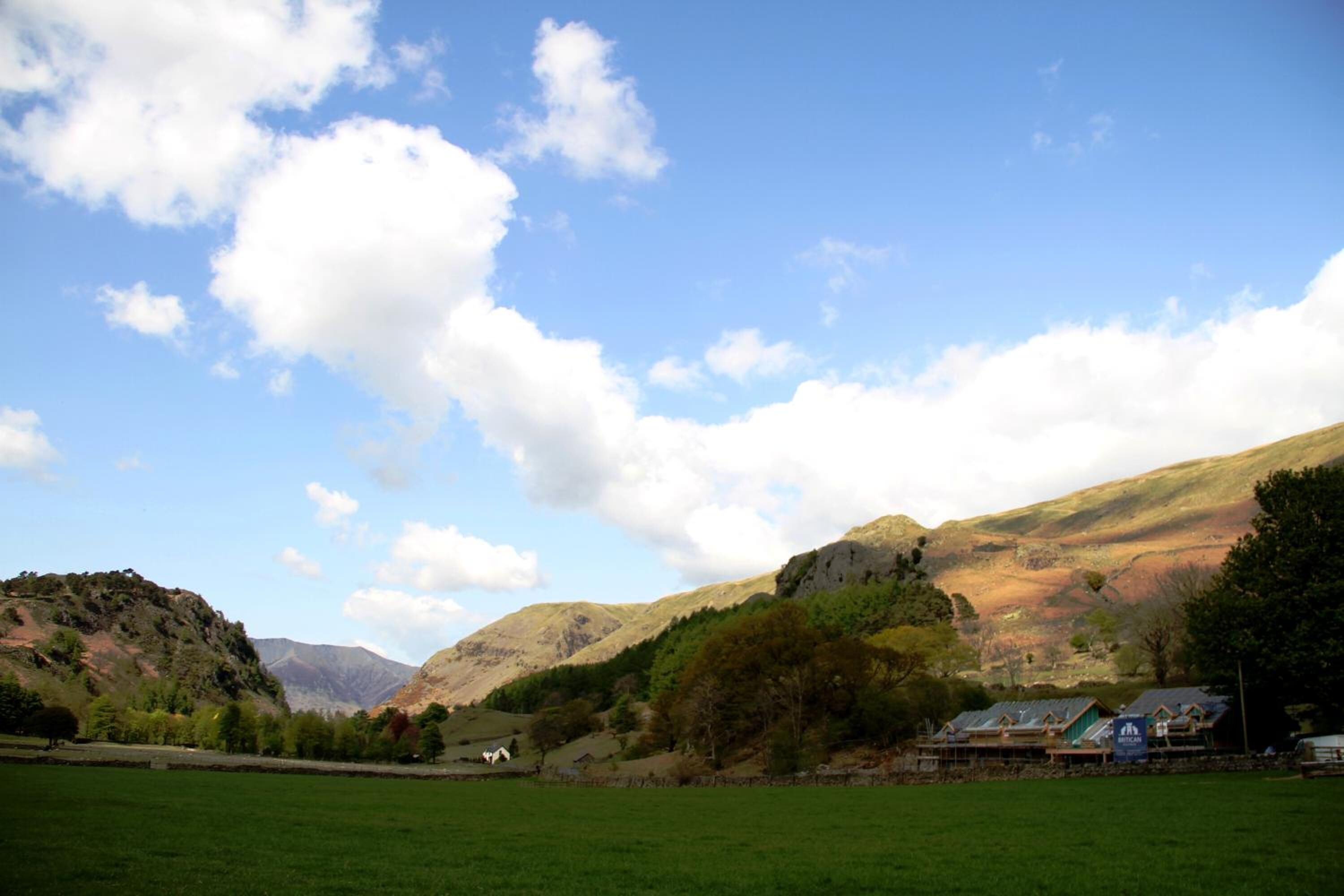 A rural landscape with a green field, a small building with a sloped roof, and a mountain in the background.