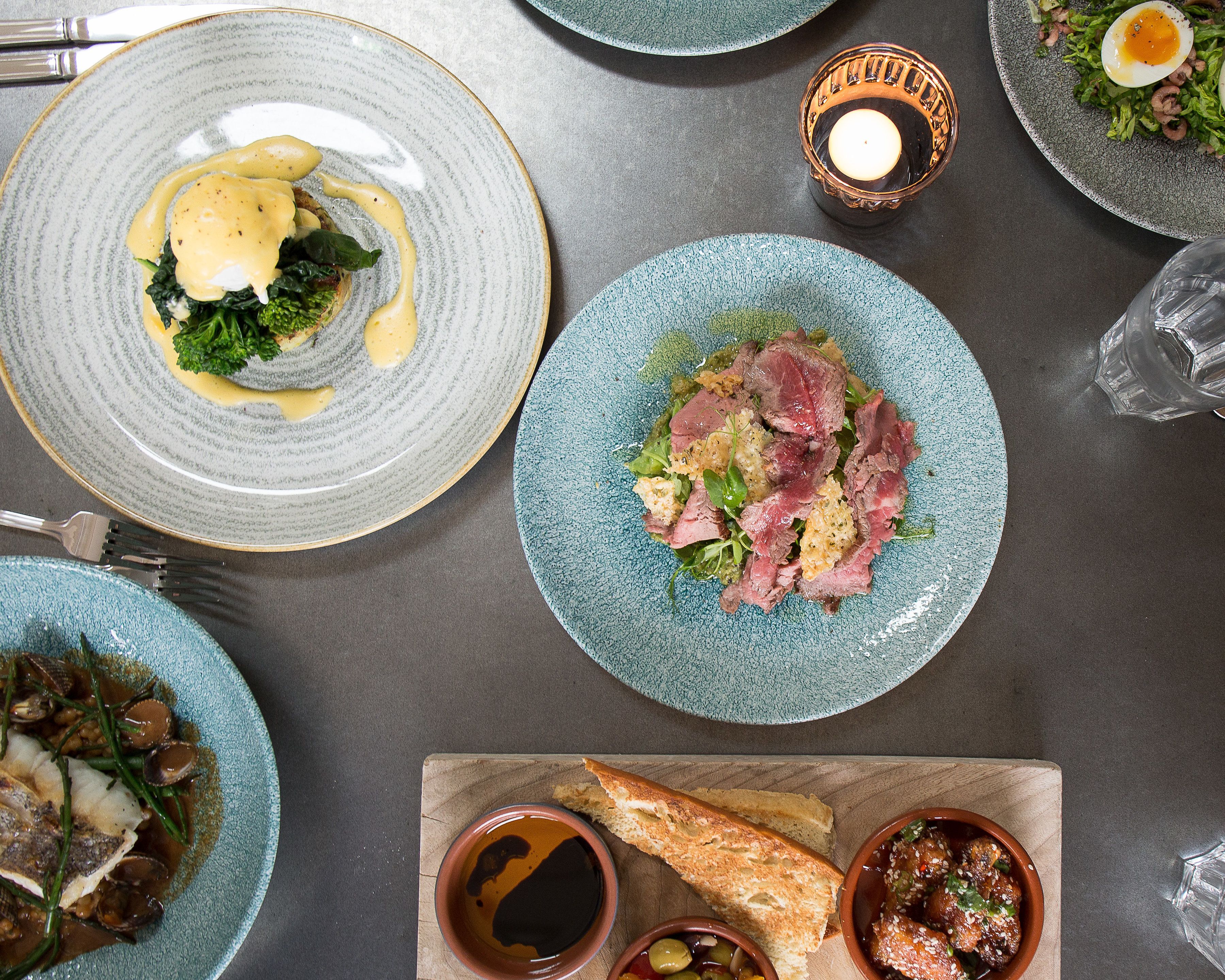 Une table à manger avec différents plats, notamment une assiette de steak, un bol de soupe et un morceau de pain.