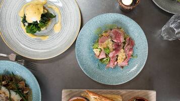 Une table à manger avec différents plats, notamment une assiette de steak, un bol de soupe et un morceau de pain.