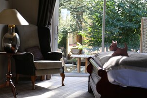 A bedroom with a bed, a chair, a lamp, and a view of a garden through a window.