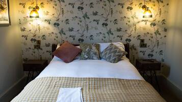 Un lit bien fait, recouvert d’une couvre-lit à motifs, deux tables de chevet avec des lampes et un papier peint à fleurs.