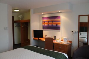 A hotel room with a bed, desk, chair, and a painting on the wall.