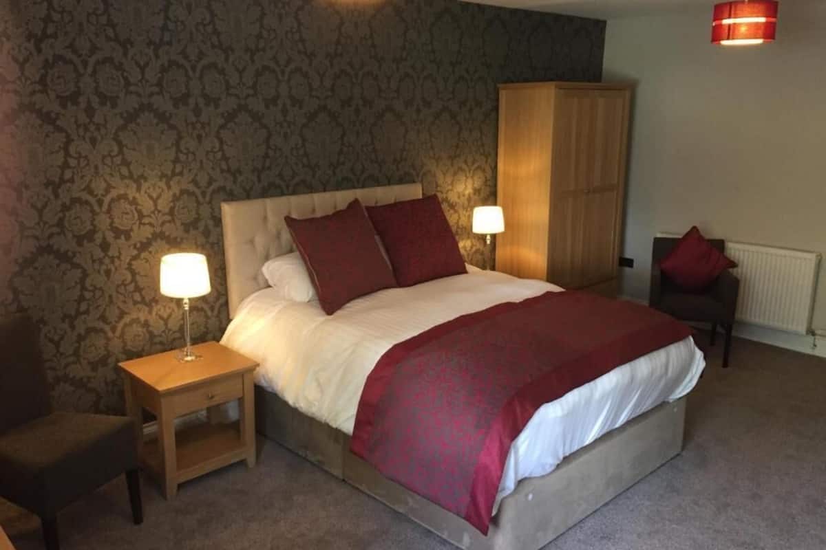 A bedroom with a large bed, two bedside lamps, a wooden nightstand, a chair, and a wardrobe.