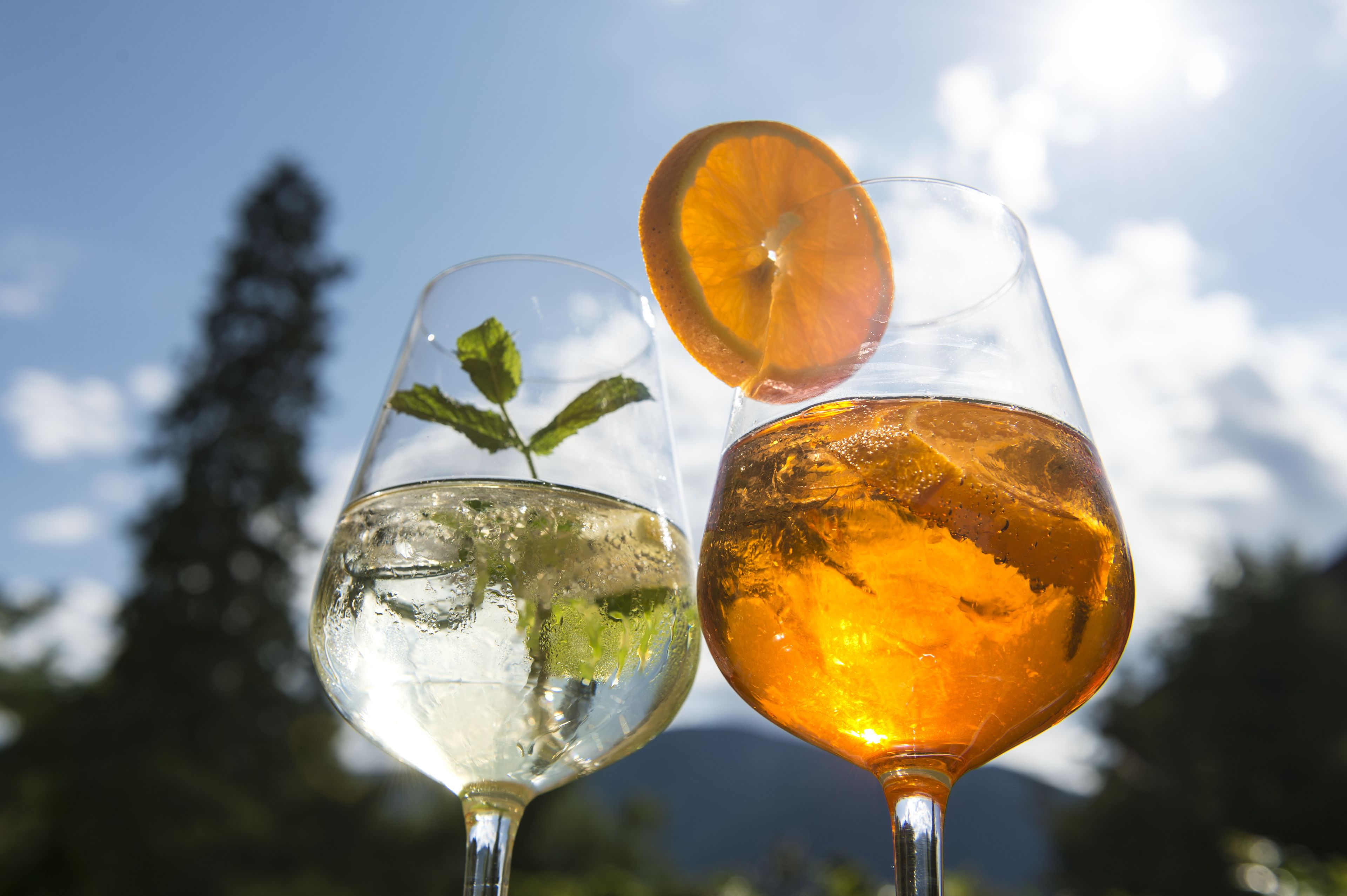 Due bicchieri di bevande guarnite con foglie di menta e fettine d'arancia, sullo sfondo di un cielo sereno.