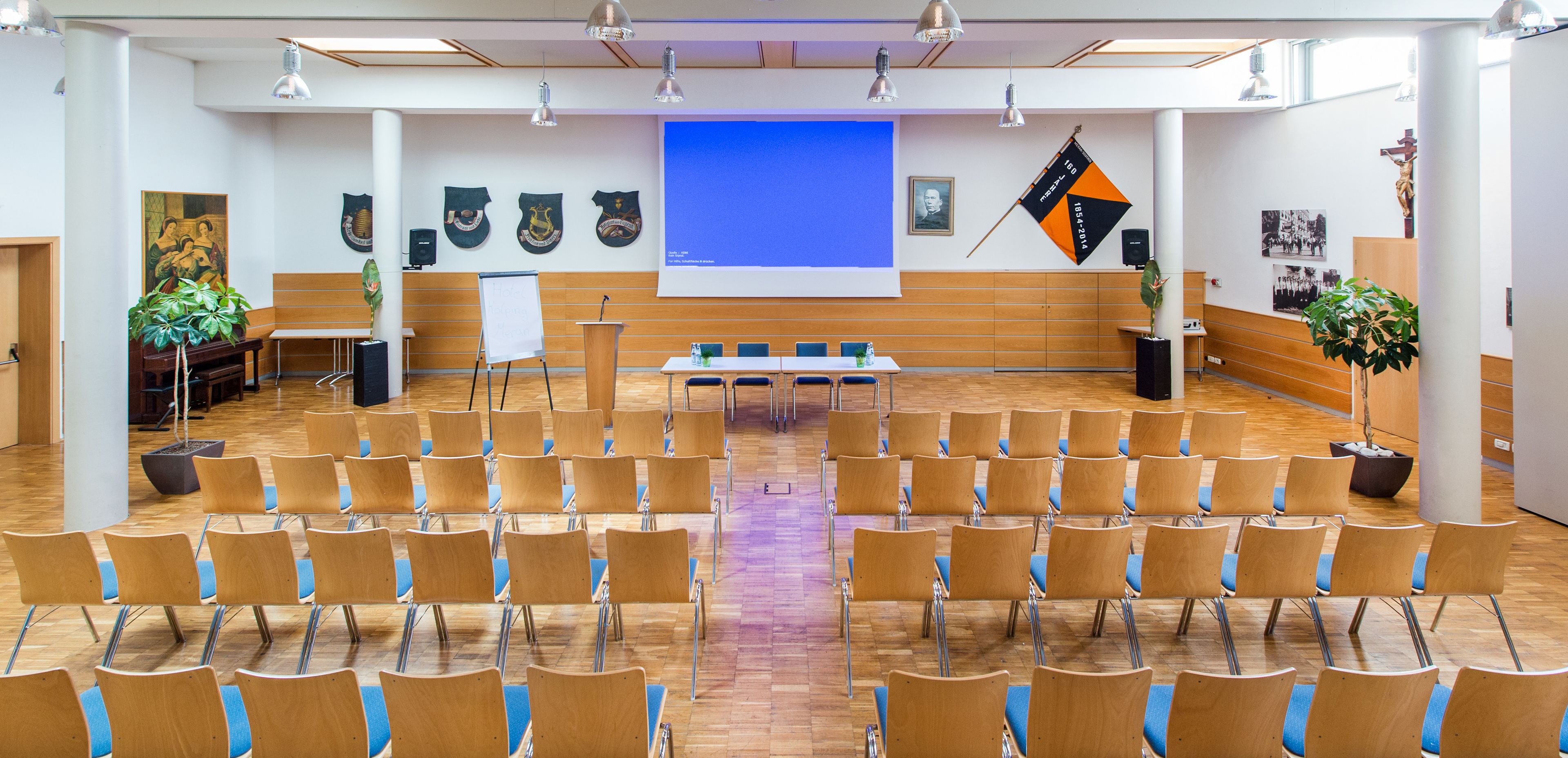 Un salón de conferencias con filas de sillas, un atril y una pantalla de proyección.
