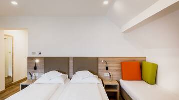 Quarto de hotel com duas camas, uma mesa de cabeceira com abajur e luminária na parede.