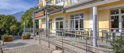 A yellow building with outdoor seating, a staircase, and a mountain in the background.