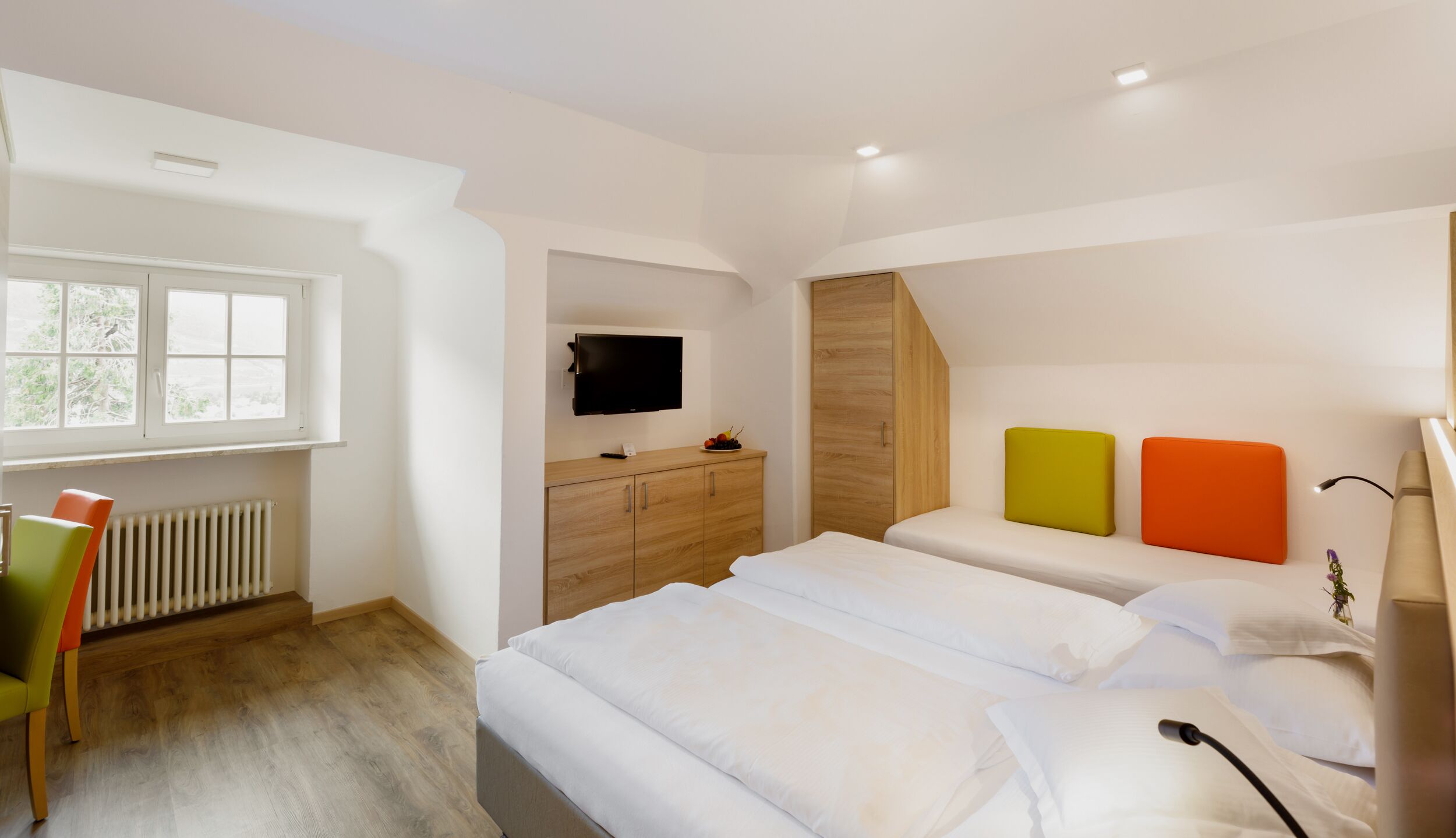 Una habitación de hotel moderna con una cama grande, televisión, un armario de madera y una ventana.