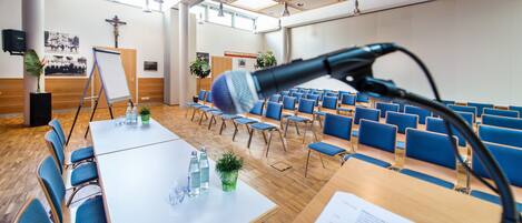 Un salón de conferencias con una pizarra, sillas azules y un micrófono.